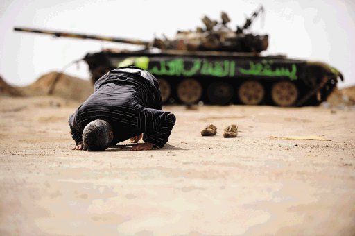 Un insurgente libio reza junto a los restos de un tanque destruído en las proximidades de Ajdabiya, Libia.  EFE.