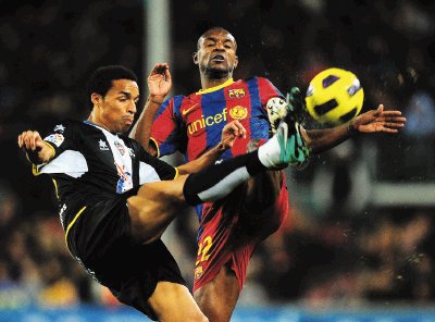 Eric Abidal y Valdo Lopes van con todo por la pelota, en un duelo re&#x00F1;ido que el Barcelona gan&#x00F3; para asegurarse el liderato. AFP