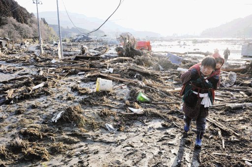 Una mujer carga a una ni&#x00F1;a para salir de la devastaci&#x00F3;n que dej&#x00F3; el tsunami. AP