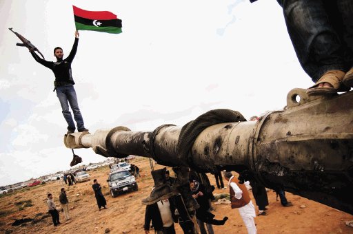 Un miliciano insurgente ondeaba la bandera de Libia encima de los restos de un carro blindado atacado anteanoche. EFE.