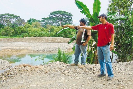 Sin rastro de pareja francesa en Quepos. Melvin Calderón y Esteban Achío señalan sitio drenado con “back hoe” en la poza del río Naranjo. C. Rodríguez.